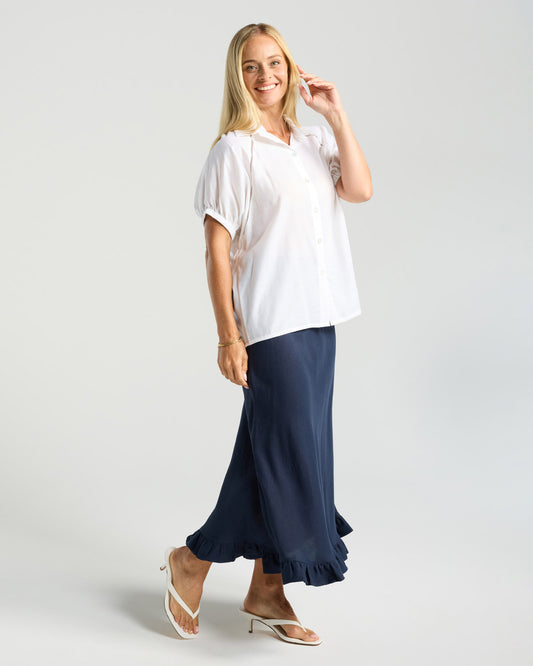 Woman wearing a white top and navy skirt on a light gray background