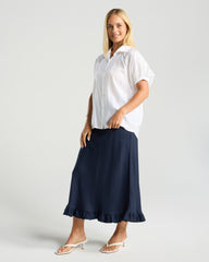Woman wearing a white shirt and navy skirt on a plain background