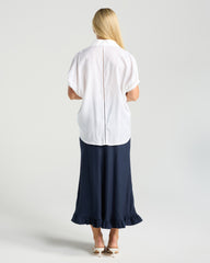 Woman wearing a white blouse and navy skirt on a plain background