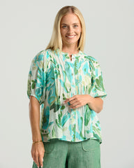 Woman wearing a tropical leaf patterned blouse against a plain background