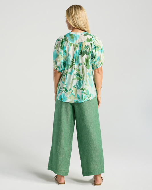 Woman wearing a floral top and green pants on a white background