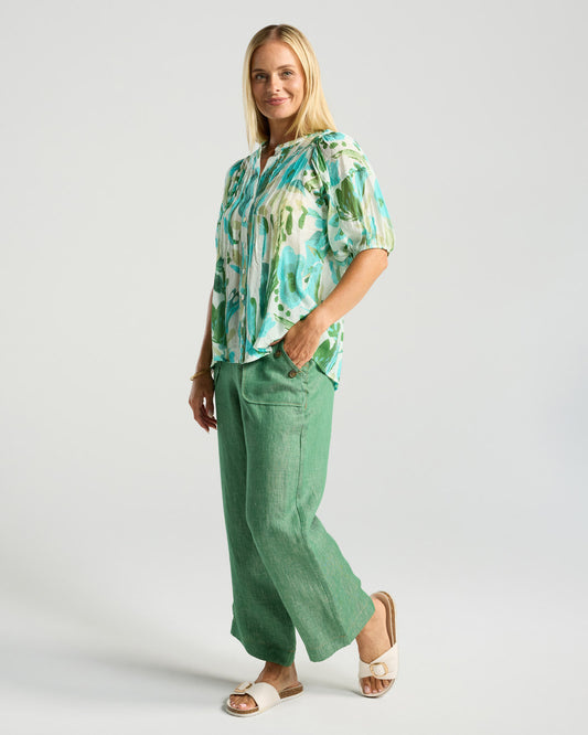 Woman wearing a floral blouse and green pants on a white background
