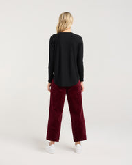 Person wearing a black long-sleeve top and burgundy pants on a white background