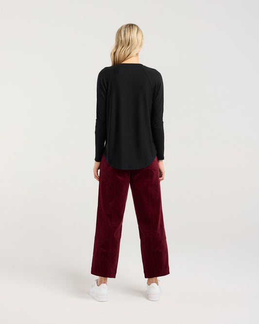 Person wearing a black long-sleeve top and burgundy pants on a white background