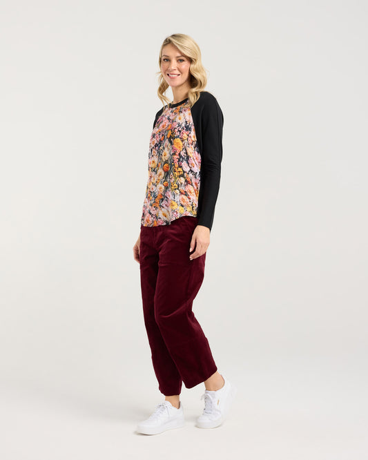 Woman wearing a floral top and burgundy pants on a white background