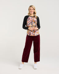 Woman wearing a floral top and burgundy pants on a white background