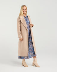 Woman wearing a long beige coat over a patterned dress on a white background
