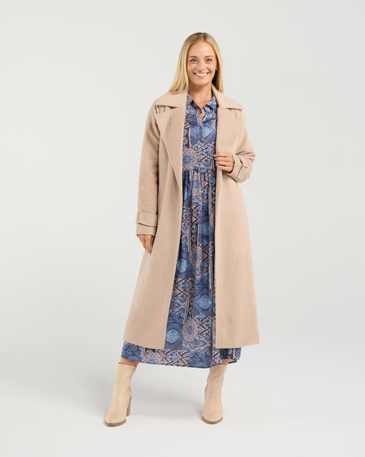 Woman wearing a long beige coat over a blue patterned dress on a white background