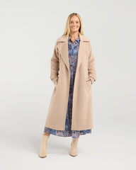 Woman wearing a beige coat over a patterned dress on a white background