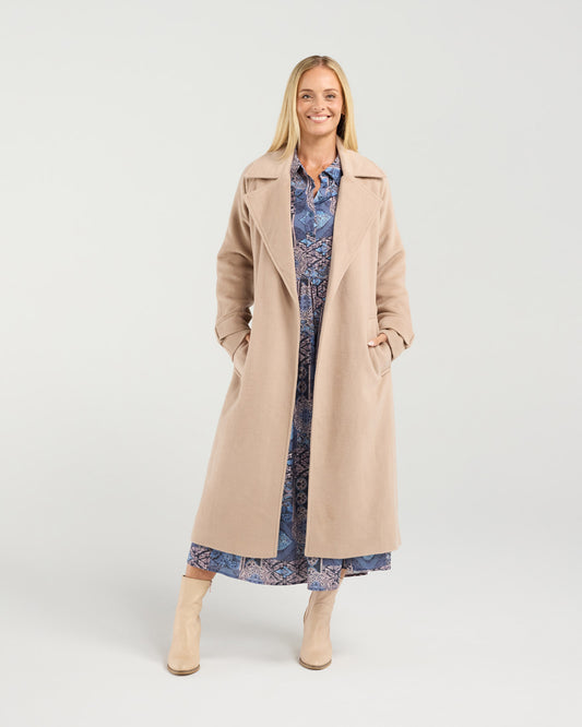 Woman wearing a beige coat over a patterned dress on a white background