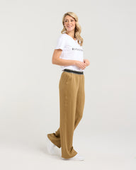 Woman wearing a white t-shirt and tan pants on a plain background