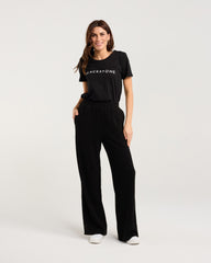 Woman wearing a black t-shirt with 'Blackstone' logo and black pants on a white background