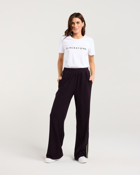 Woman wearing a white t-shirt with 'Blackstone' logo and black pants on a white background