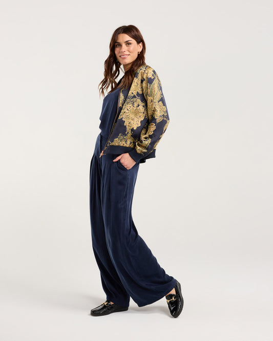 Woman wearing a patterned jacket and navy pants on a white background