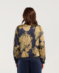 Woman wearing a gold and navy floral blouse with wide-leg navy pants on a white background