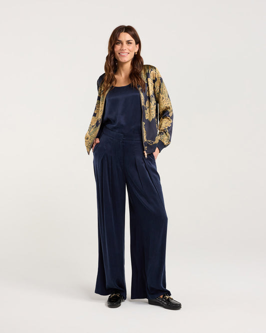 Woman wearing a patterned jacket and navy jumpsuit on a white background