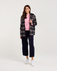 Woman wearing a plaid shirt, pink sweater, and navy pants on a white background