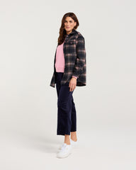Woman wearing a plaid shirt over a pink top and navy pants on a light gray background