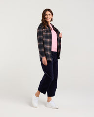 Woman wearing a plaid shirt over a pink top with navy pants on a white background