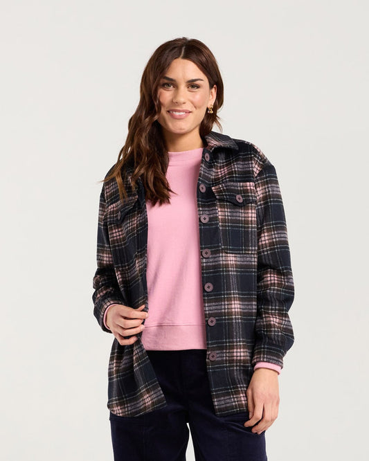 Woman wearing a plaid shirt, pink sweater, and dark pants on a white background