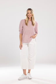 Woman wearing a patterned pink blouse and white pants on a white background