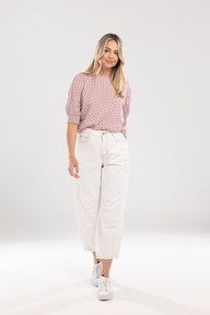 Woman wearing a pink patterned blouse and white pants on a white background