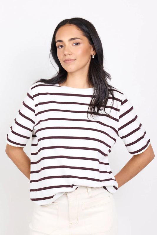 Woman wearing a white and brown striped shirt against a plain background