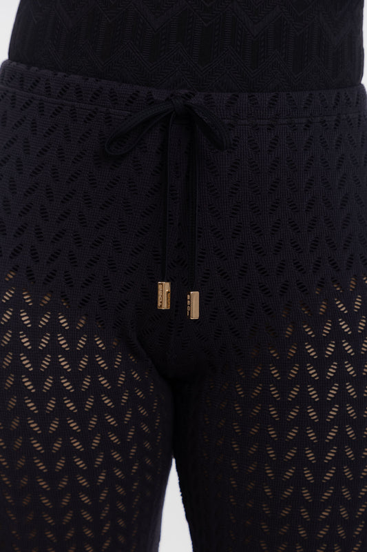Close-up of black textured knit leggings with a drawstring waist and gold-toned hardware, shown on a model against a light gray background.