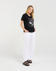 Woman wearing a black t-shirt with a graphic design and white pants on a white background