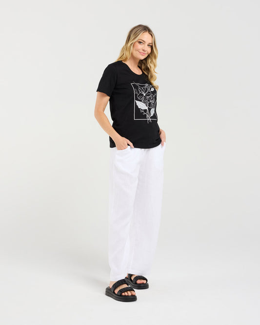 Woman wearing a black t-shirt with a graphic design and white pants on a white background