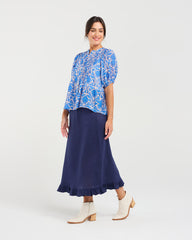 Woman wearing a blue floral blouse and navy skirt on a white background