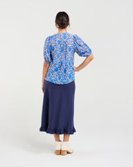 Woman wearing a blue patterned top and navy skirt on a white background