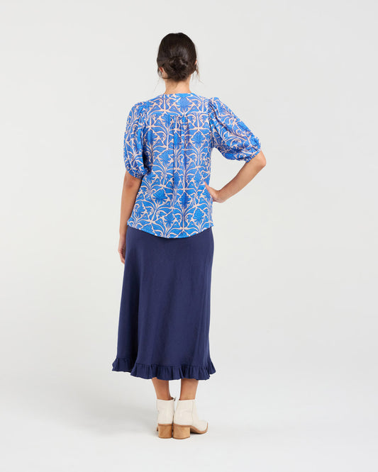 Woman wearing a blue patterned top and navy skirt on a white background