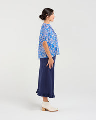 Woman wearing a blue floral blouse and navy skirt on a white background
