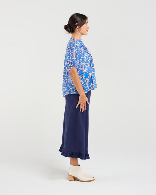 Woman wearing a blue floral blouse and navy skirt on a white background
