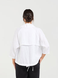 Person wearing a white jacket and black pants on a plain background