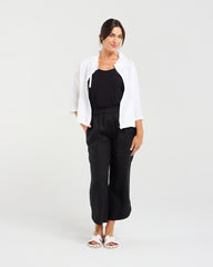 Woman wearing a white jacket and black pants on a plain background