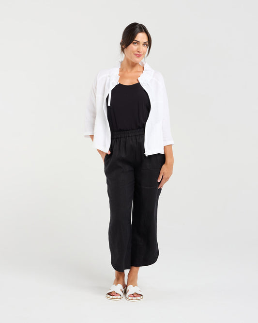 Woman wearing a white jacket and black pants on a plain background