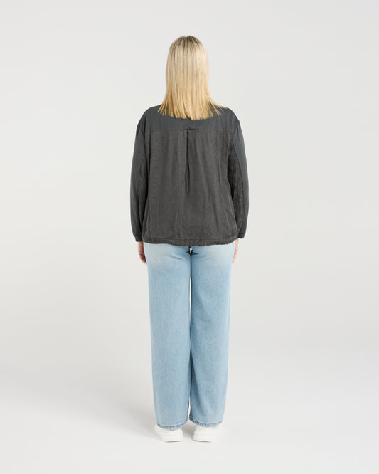 Person wearing a dark gray long-sleeve shirt and light blue jeans on a white background