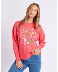 Woman wearing a pink sweatshirt with floral design and 'FOXWOOD' branding on a light gray background