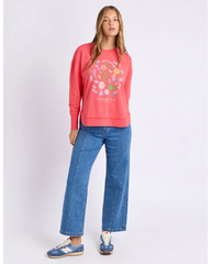 Woman wearing a coral sweatshirt with floral design and blue jeans on a white background