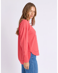 Woman wearing a coral sweatshirt and blue jeans on a light gray background