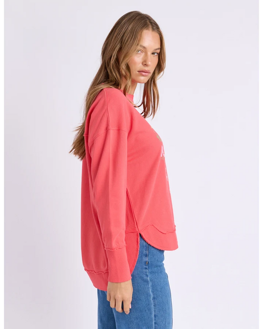 Woman wearing a coral sweatshirt and blue jeans on a light gray background