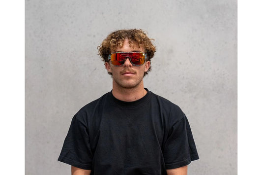 Person wearing a black t-shirt and colorful sunglasses against a gray background