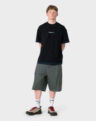 Person wearing a black t-shirt with a logo and green shorts on a white background