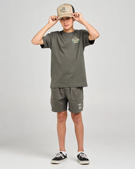 Person wearing a green t-shirt and shorts set with a beige cap on a light gray background