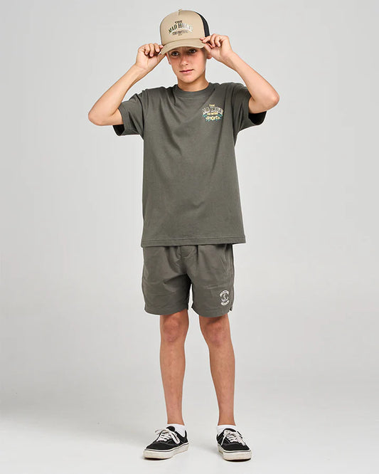 Person wearing a green t-shirt and shorts set with a beige cap on a light gray background