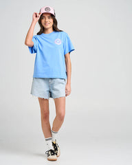 Person wearing a light blue t-shirt, denim shorts, and a pink cap on a plain background