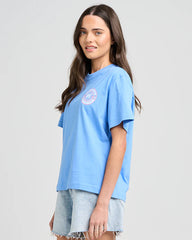 Woman wearing a light blue t-shirt with a logo on a plain background