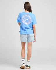 Person wearing a blue t-shirt with a logo on the back, standing against a plain background